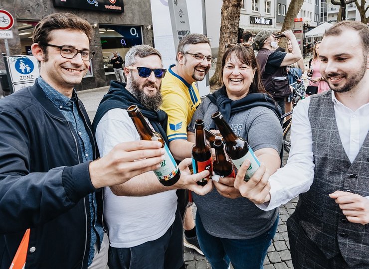 Fünf Personen halten ihre Bierflaschen in die Kamera und erfreuen sich sichtlich.