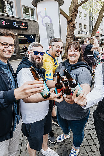 Fünf Personen halten ihre Bierflaschen in die Kamera und erfreuen sich sichtlich.