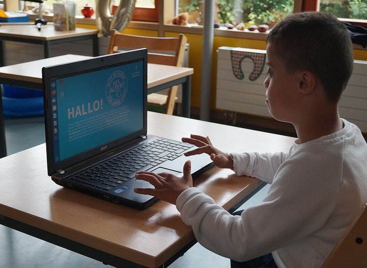 Ein dunkelhäutiger Junge sitzt vor einem Computer.