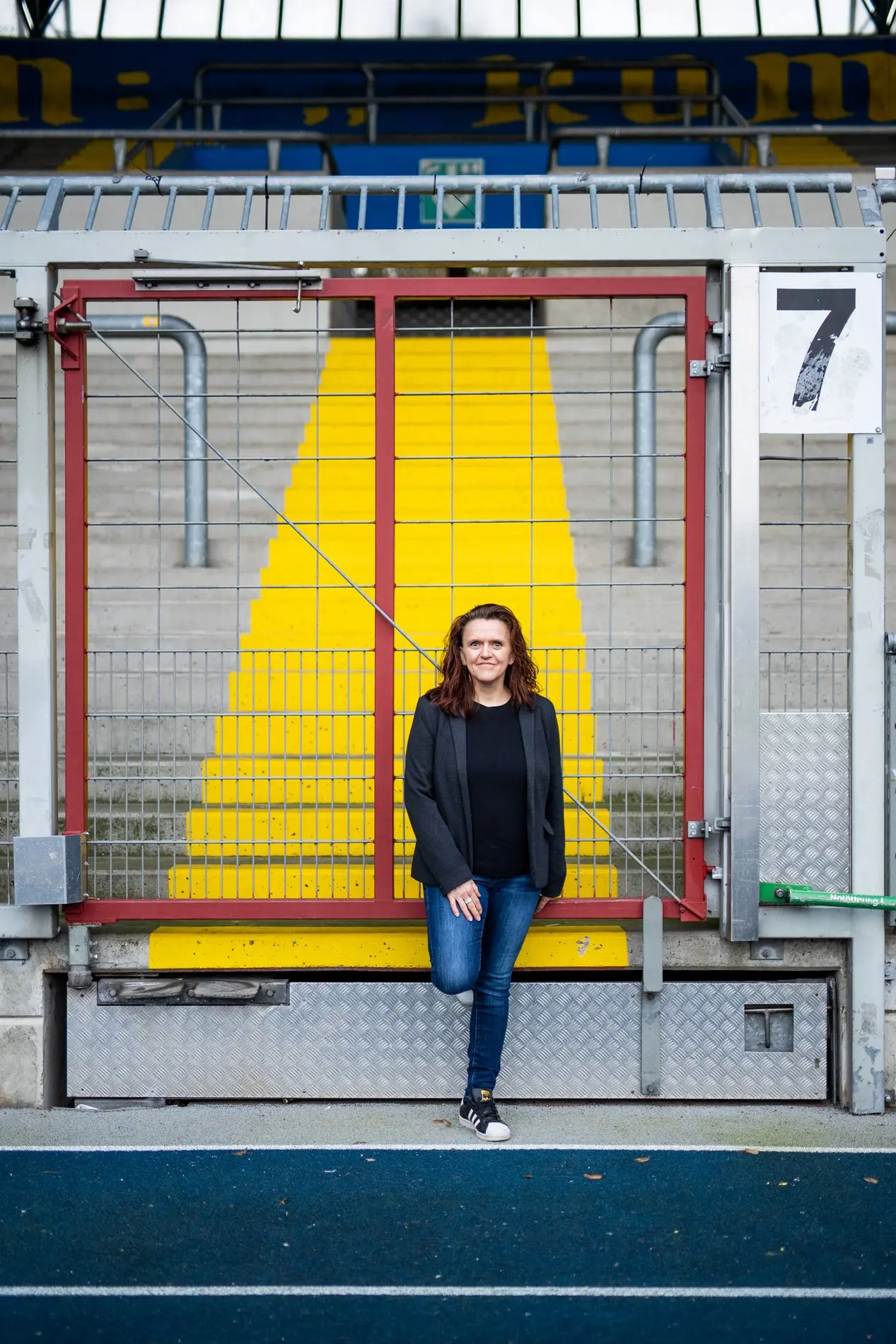 Eine Frau steht vor der Treppe einer Fußballtribüne.