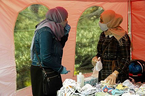 Zwei Muslima mit Kopftuch und Mundschutz unterhalten sich.