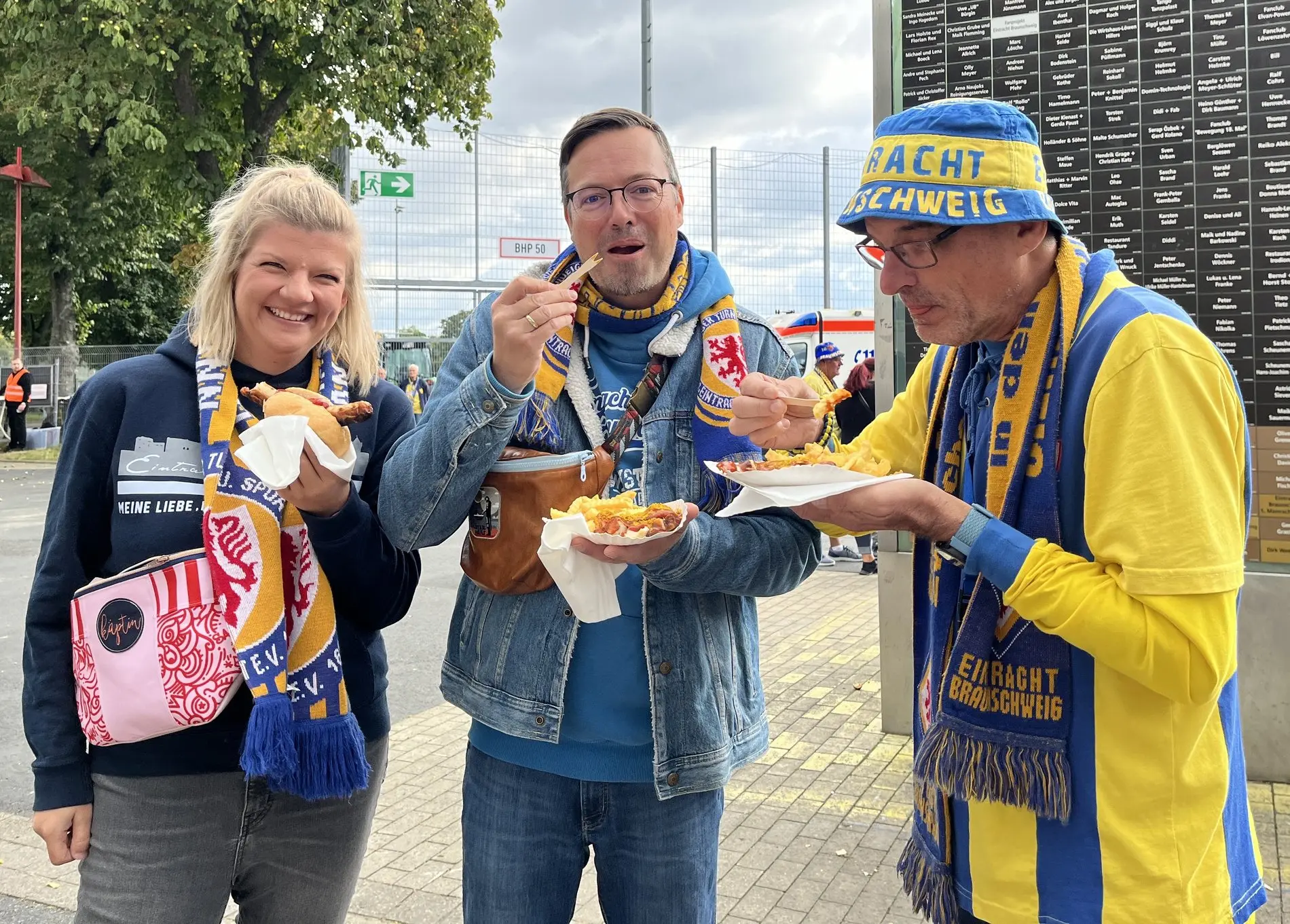 Drei Fans stärken sich vor der „Hall of Fans“ mit Pommes und Wurst.