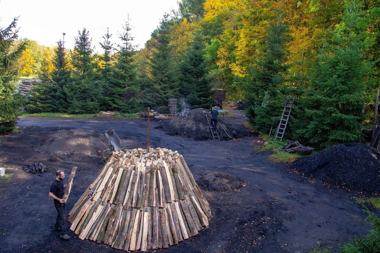 Männer schichten einen Haufen aus langen Holzscheiten auf.