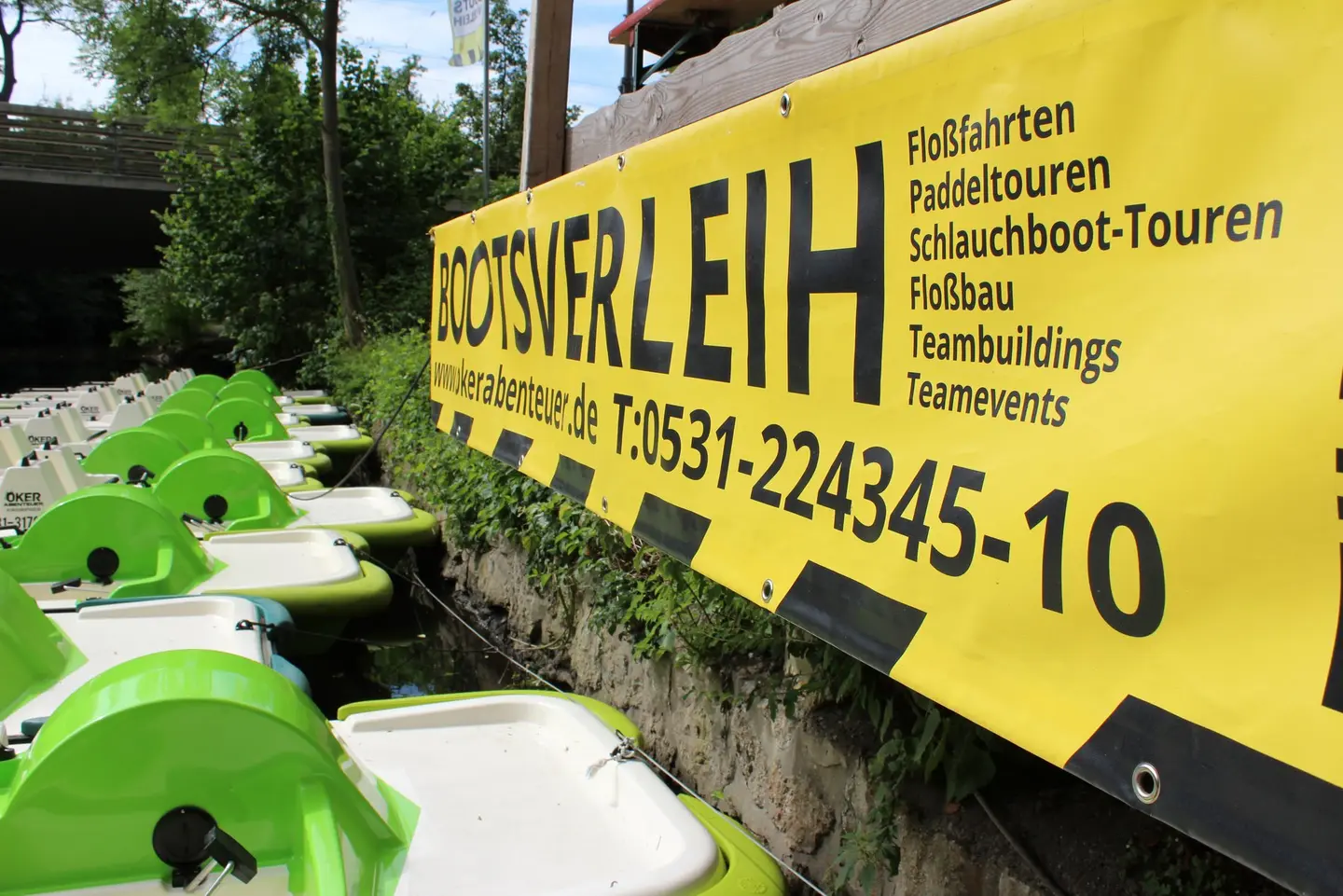 Tretboote im Wasser, darüber ein gelbes Plakat.