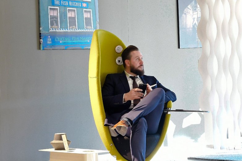 Ein Mann sitzt auf einem gelben Drehstuhl mit umschließender Lehne.