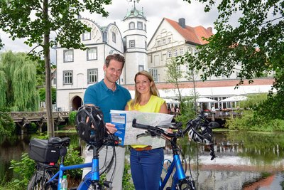 Zwei Personen stehen neben blauen Fahrrädern und halten eine Karte in der Hand. Im Hintergrund ist das Welfenschloss zu sehen.