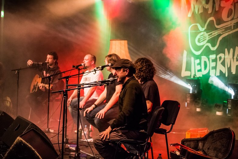 Fünf Musiker sitzen auf Stühlen am vorderen Rand der Bühne und singen in Mikrofone. 