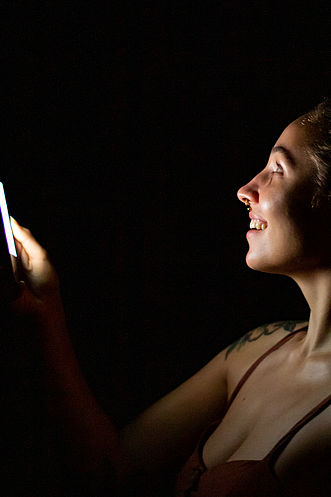 Eine junge Frau schaut im Dunkeln auf ihr Smartphone.