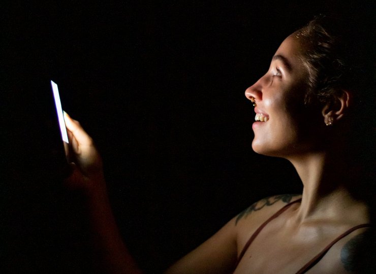 Eine junge Frau schaut im Dunkeln auf ihr Smartphone.