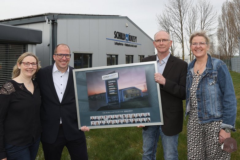 Zwei Paare stehen jeweils seitlich von einem Firmenbild