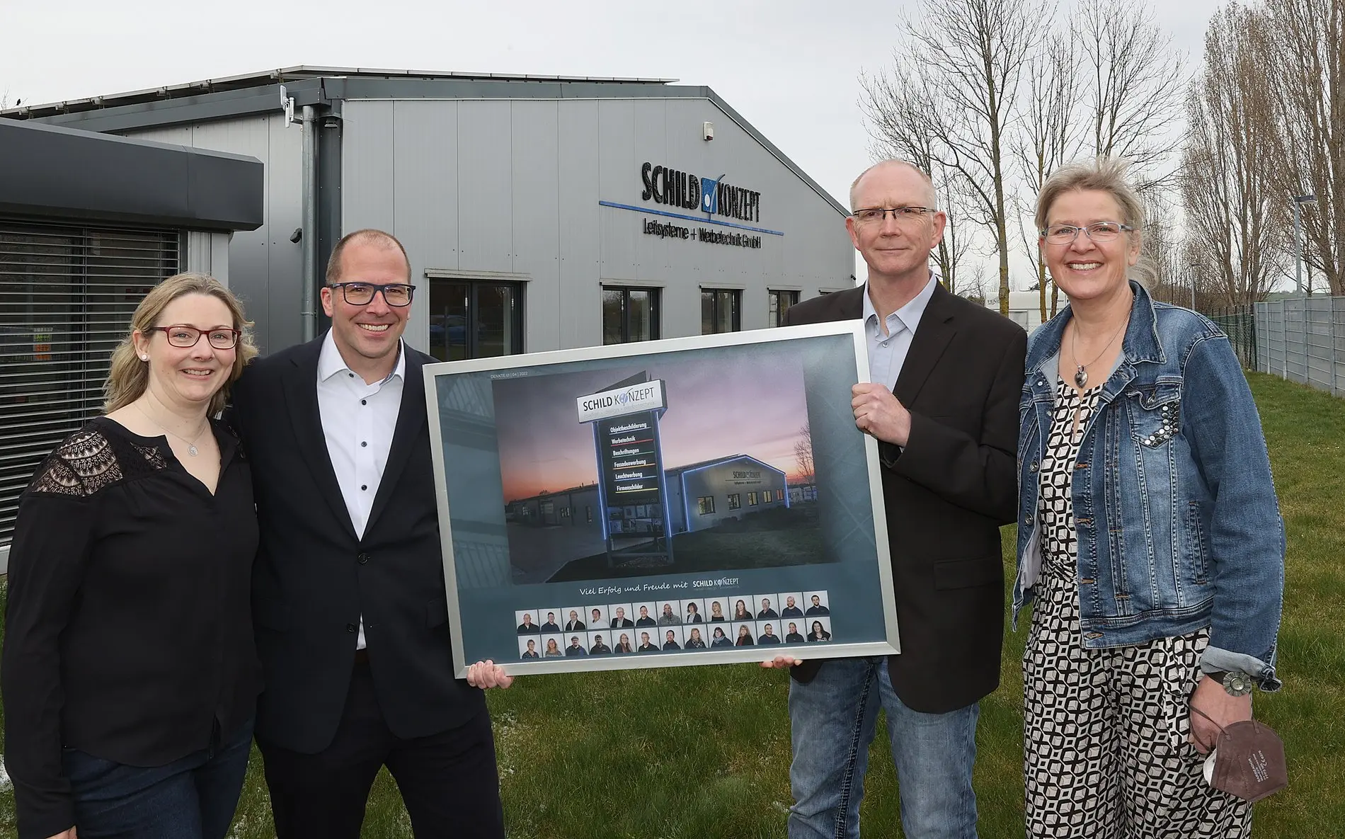 Zwei Paare stehen jeweils seitlich von einem Firmenbild