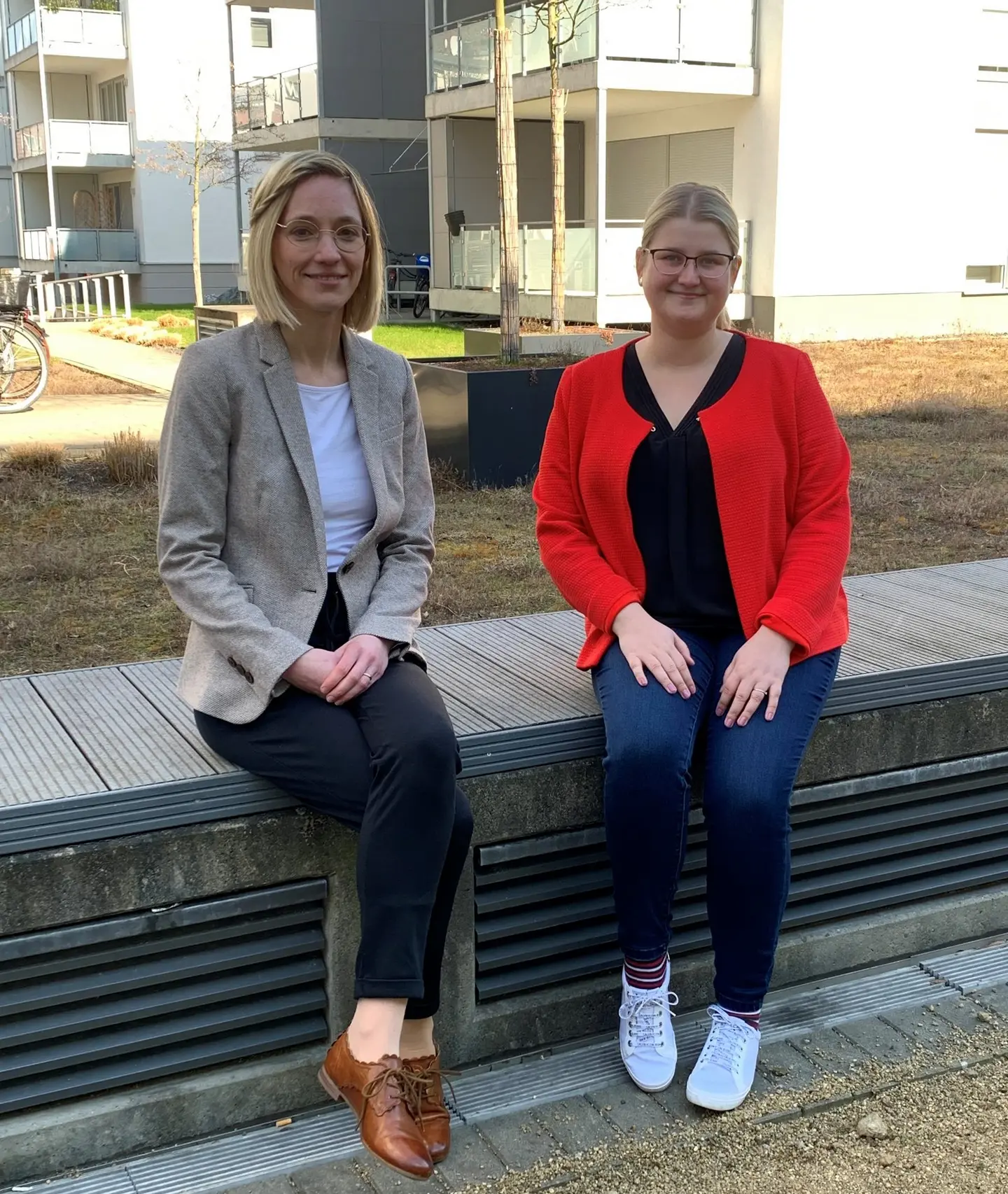 Zwei Frauen sitzen auf einer niedrigen Mauer.