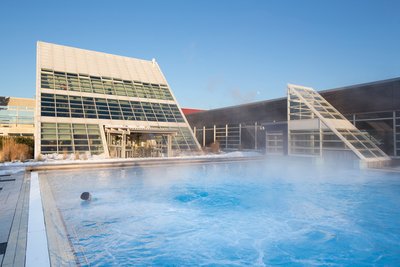 Man blickt auf das Außenbecken des Thermalsolbad. Links und rechts hinter dem Becken sieht man die dreieckförmigen Aufbauten der Schwimmhalle.