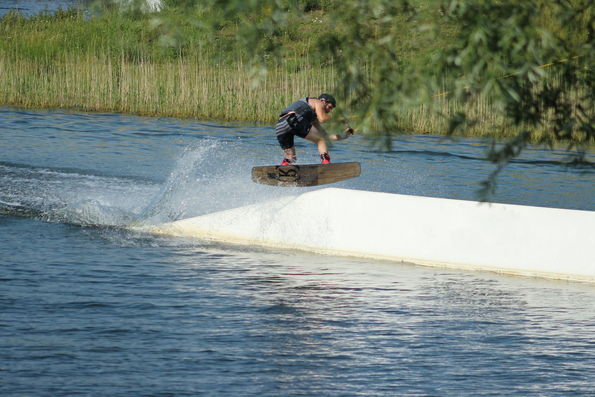 Ein Wakeboarder springt über eine Rampe im Wasser des Allersees. 