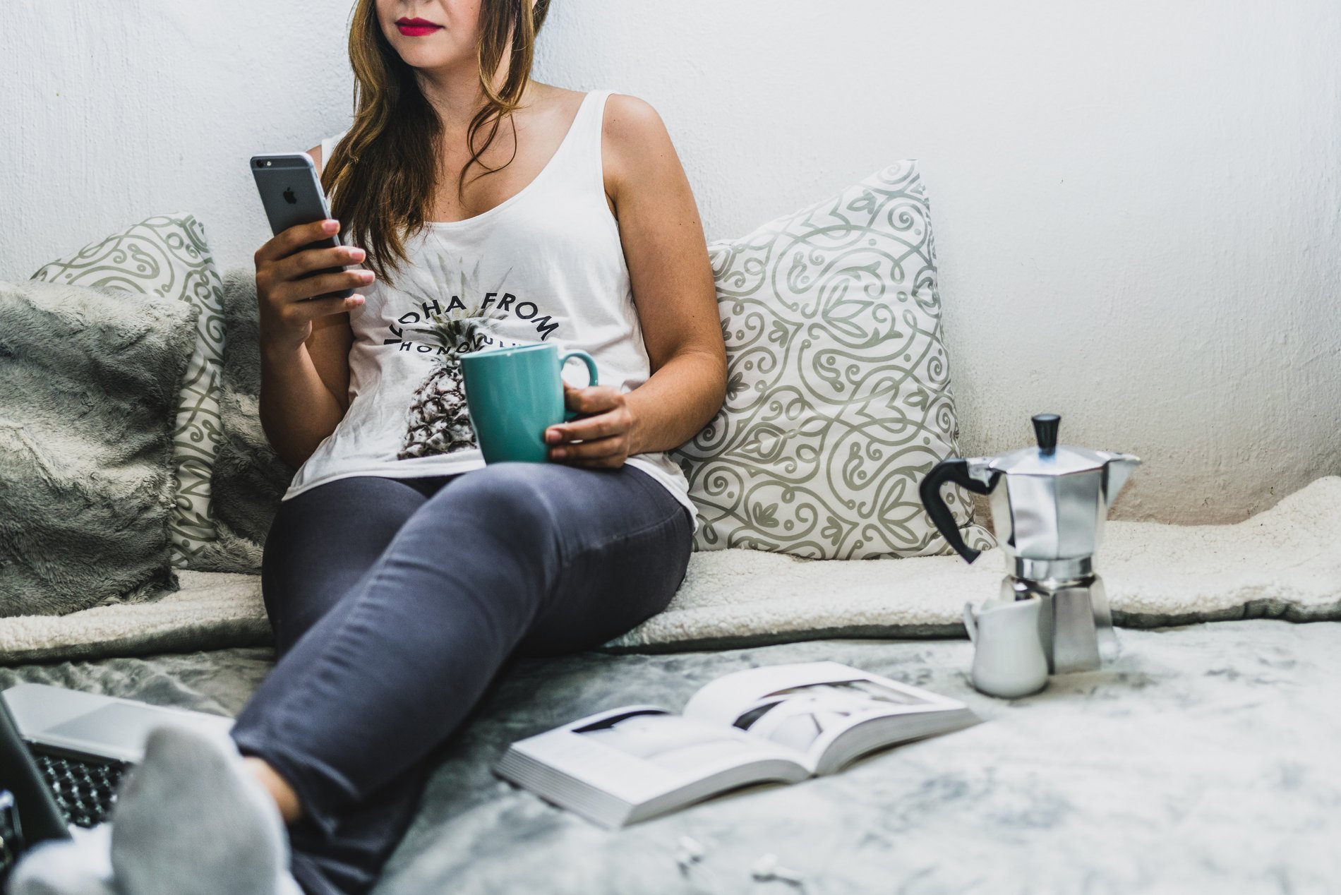 Eine Frau sitzt mit Kopfhörer und Smartphone auf einem Bett.