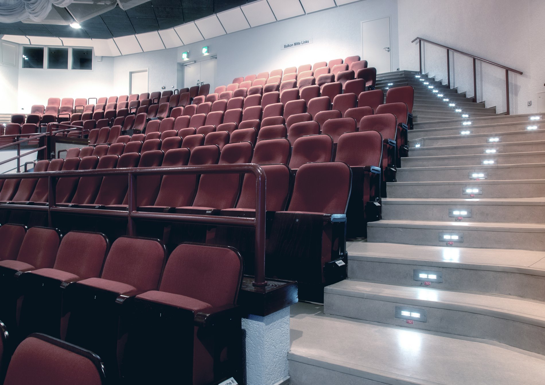 Der große, leere Saal des CongressPark Wolfsburg mit roten Klappsitzen, eine Treppe führt daran rechts vorbei nach oben.