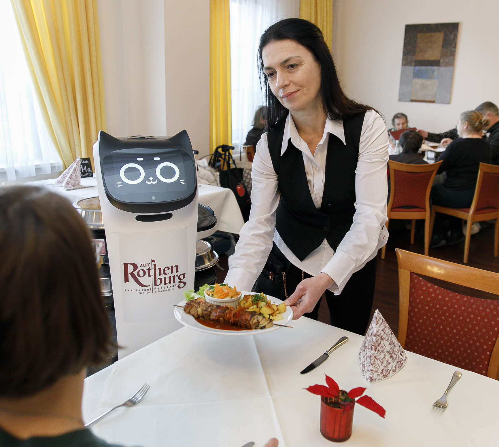 Eine Kellnerin serviert Essen, ein Roboter steht daneben.