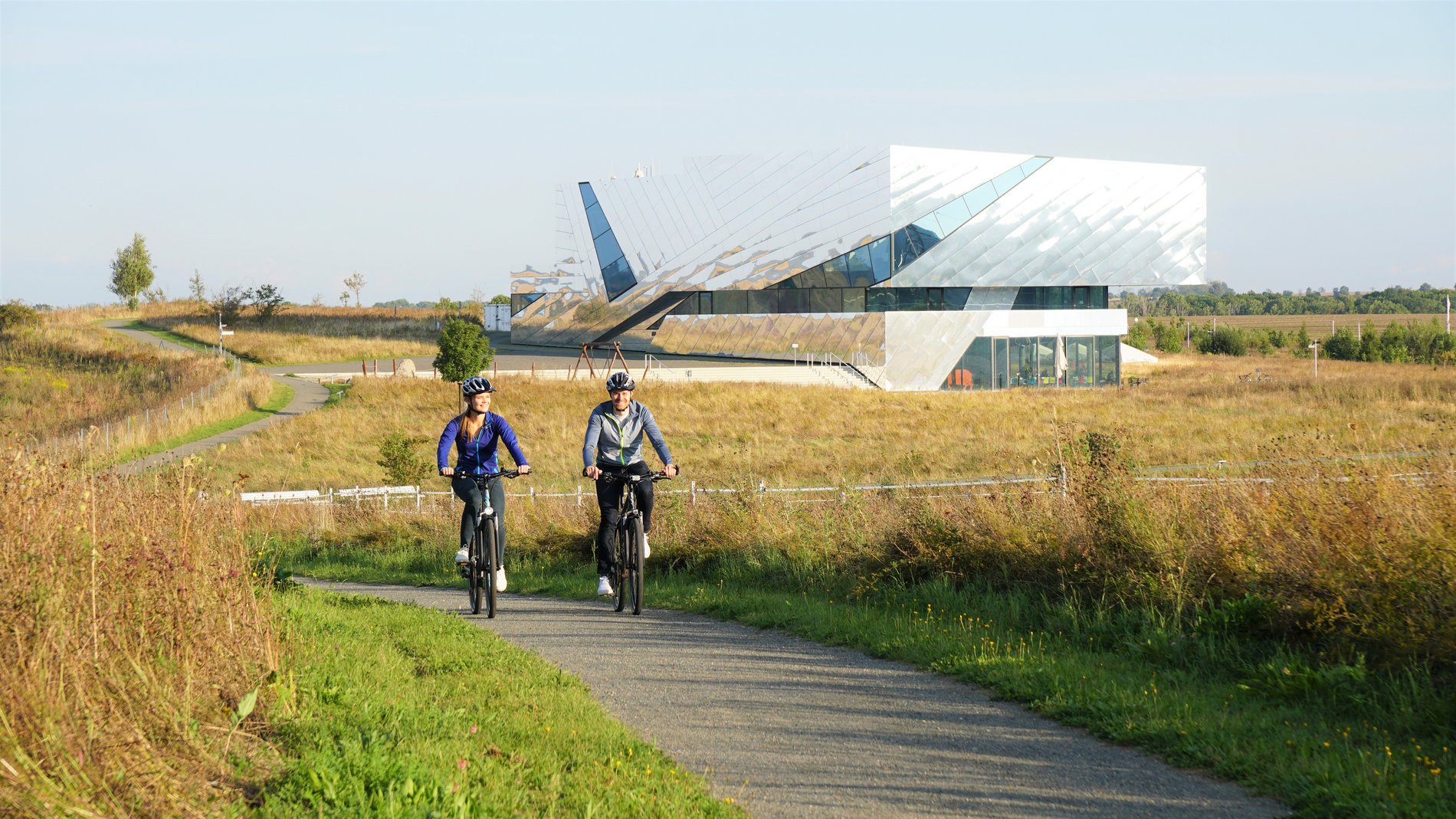 Zwei Menschen beim Fahrradfahren im Landkreis Helmstedt, im Hintergrund das Forschungsmuseum Schöningen, bekannt als Paläon.       