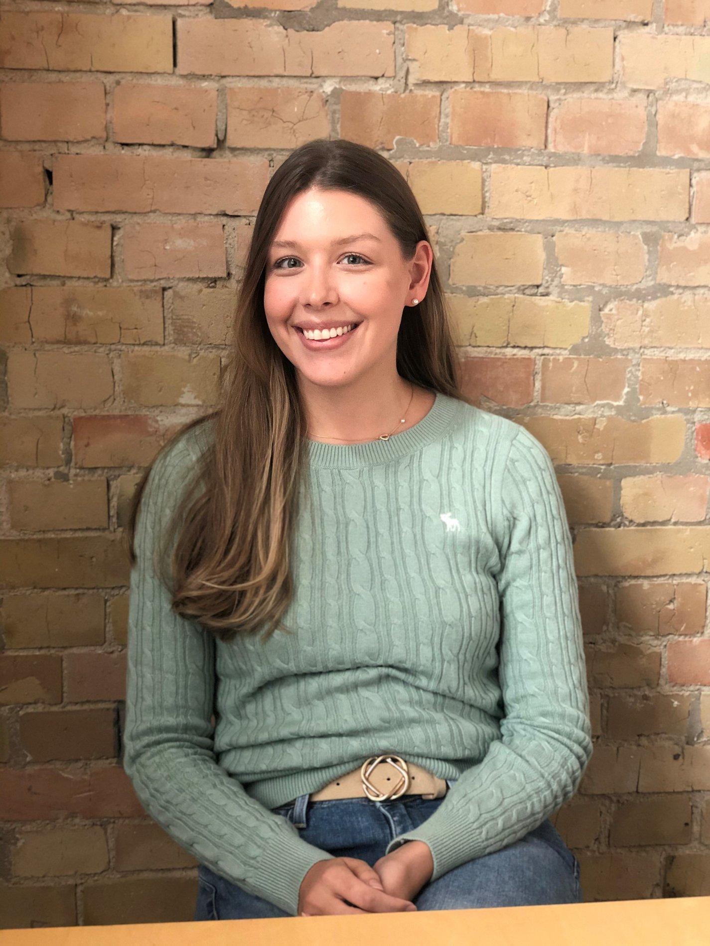 Eine junge Frau sitzt vor einer Backsteinwand.
