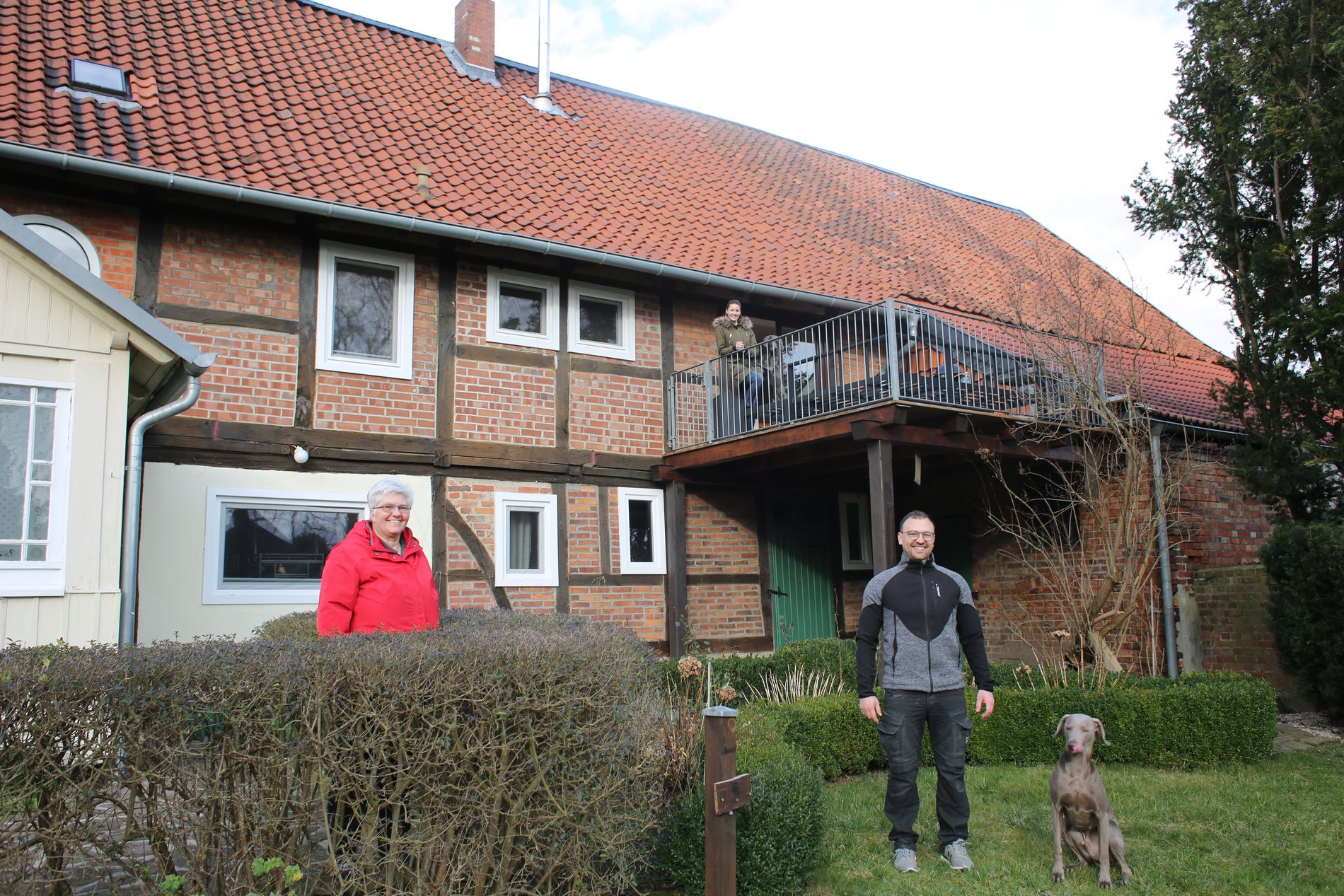 Drei Personen stehen vor einem Bauernhaus.