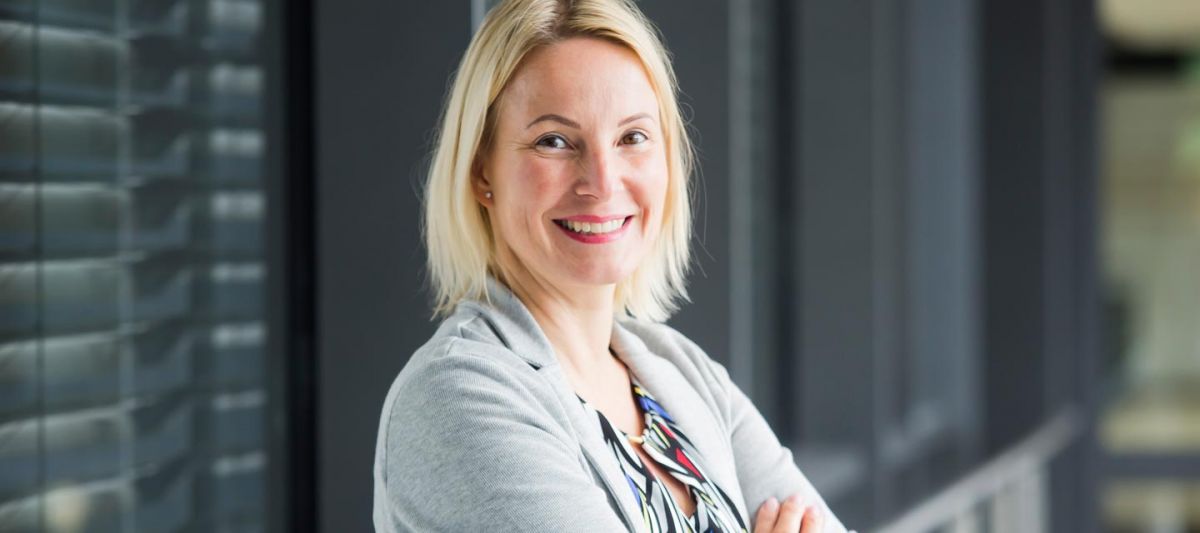 Blone Dame mit verschränkten Arbmen lacht in die Kamera