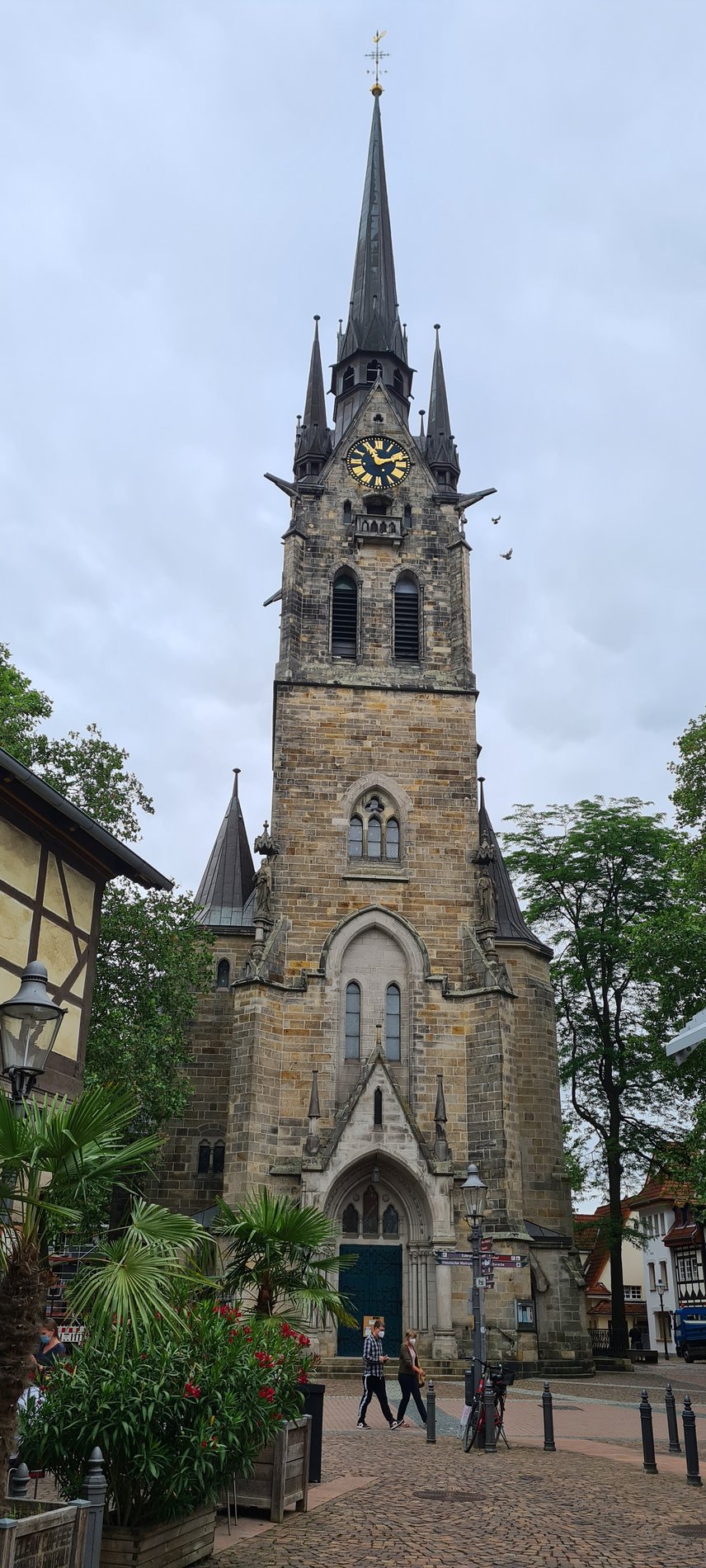 Man blickt frontal auf einen alten Kirchturm aus Stein. Im oberen Teil des Turms ist eine Uhr zu sehen.