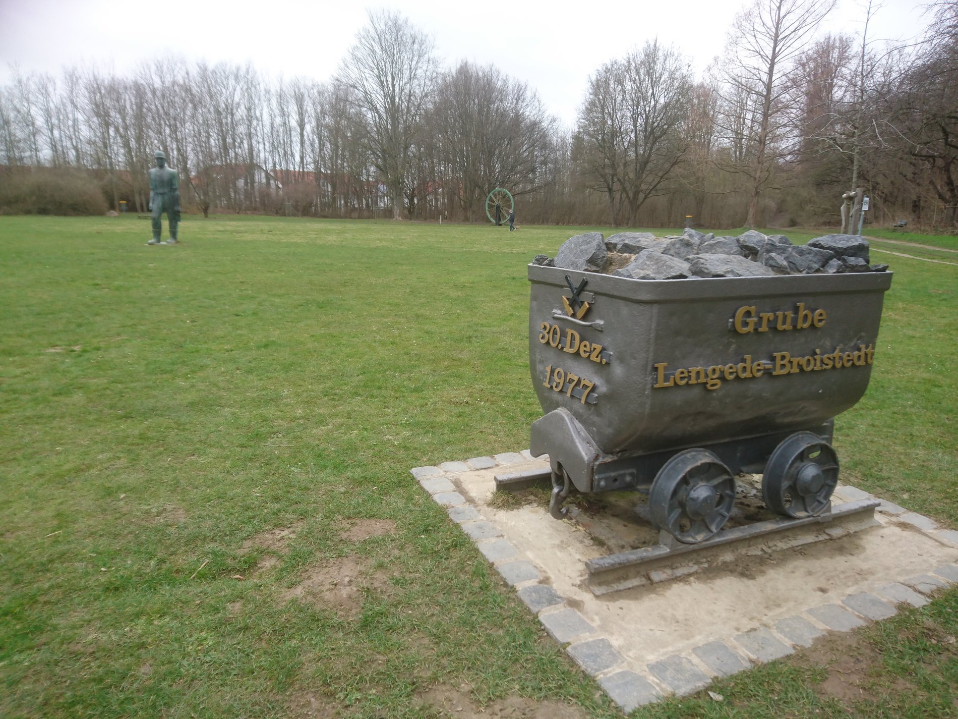 Man blickt auch die Bronzestatue einer Lore auf Schienen. Auf der Lore steht: "Grube Lengede-Broistedt" und "30. Dez. 1977". 