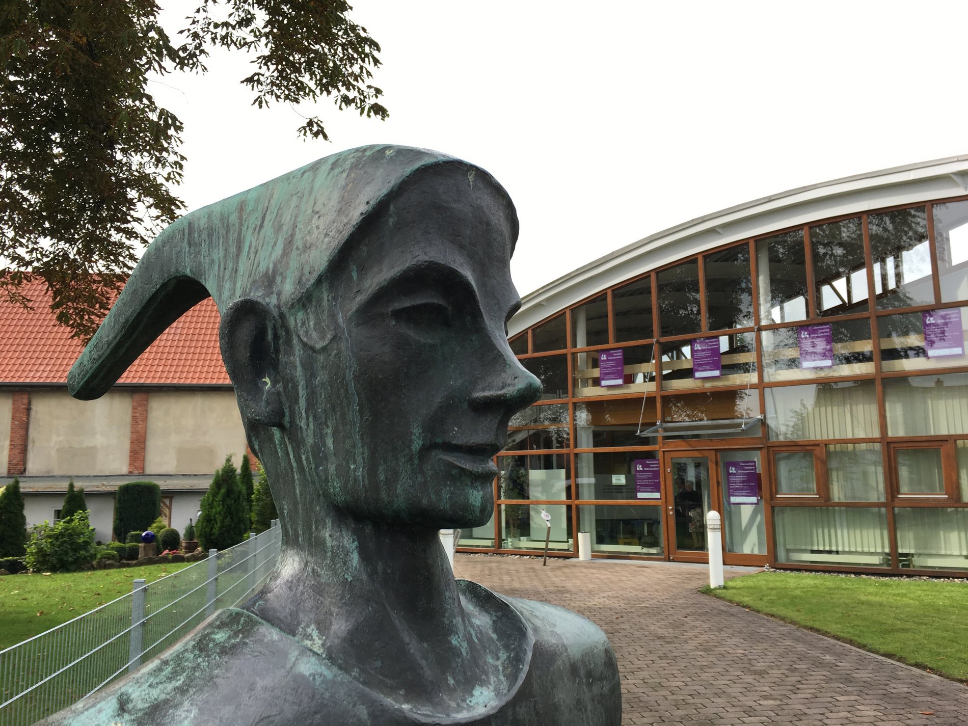 Man blickt auf eine Bronzestatue von Till Eulenspiegel, dahinter das Eulenspiegelmuseum