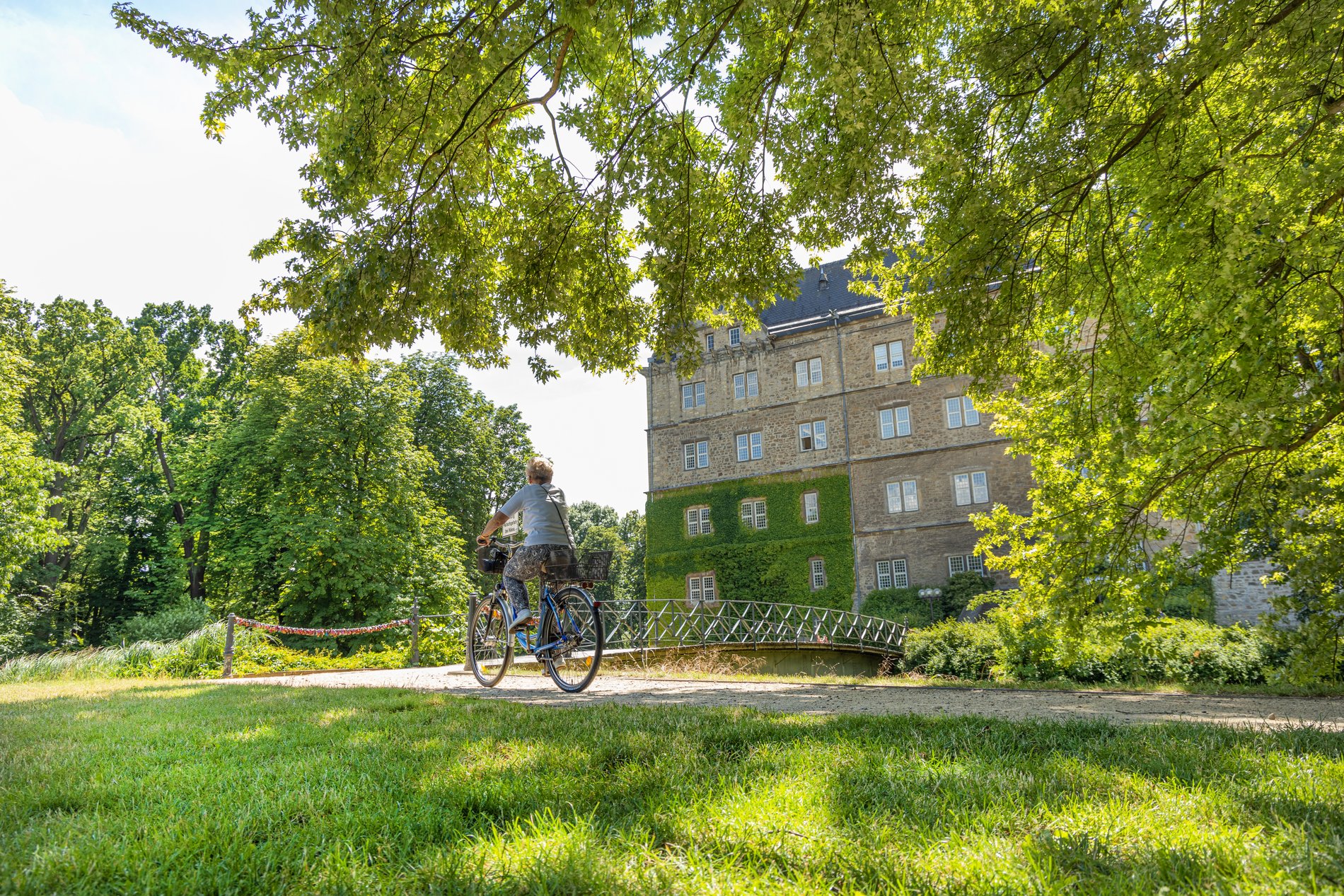 Man blickt auf einen Radfahrer, der durch eine Parkanlage am Schloss Fallersleben fährt.