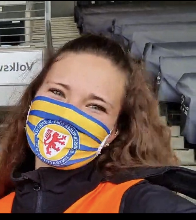 Eine Frau mit Eintracht-Braunschweig-Mundschutz.