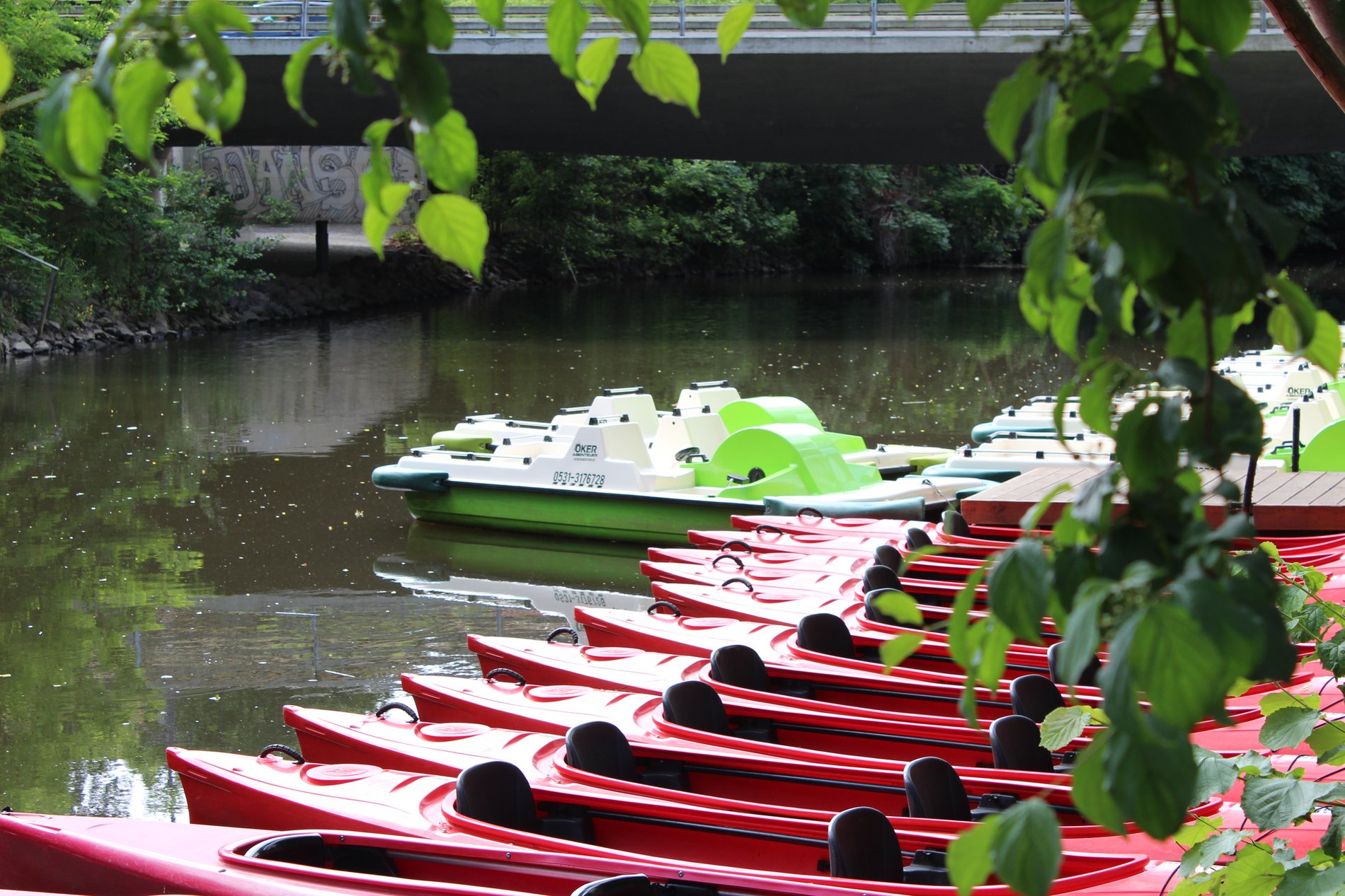 Eine Reihe schmaler roter Zweisitzer-Boote liegt im Wasser an der Floßstation Braunschweig.