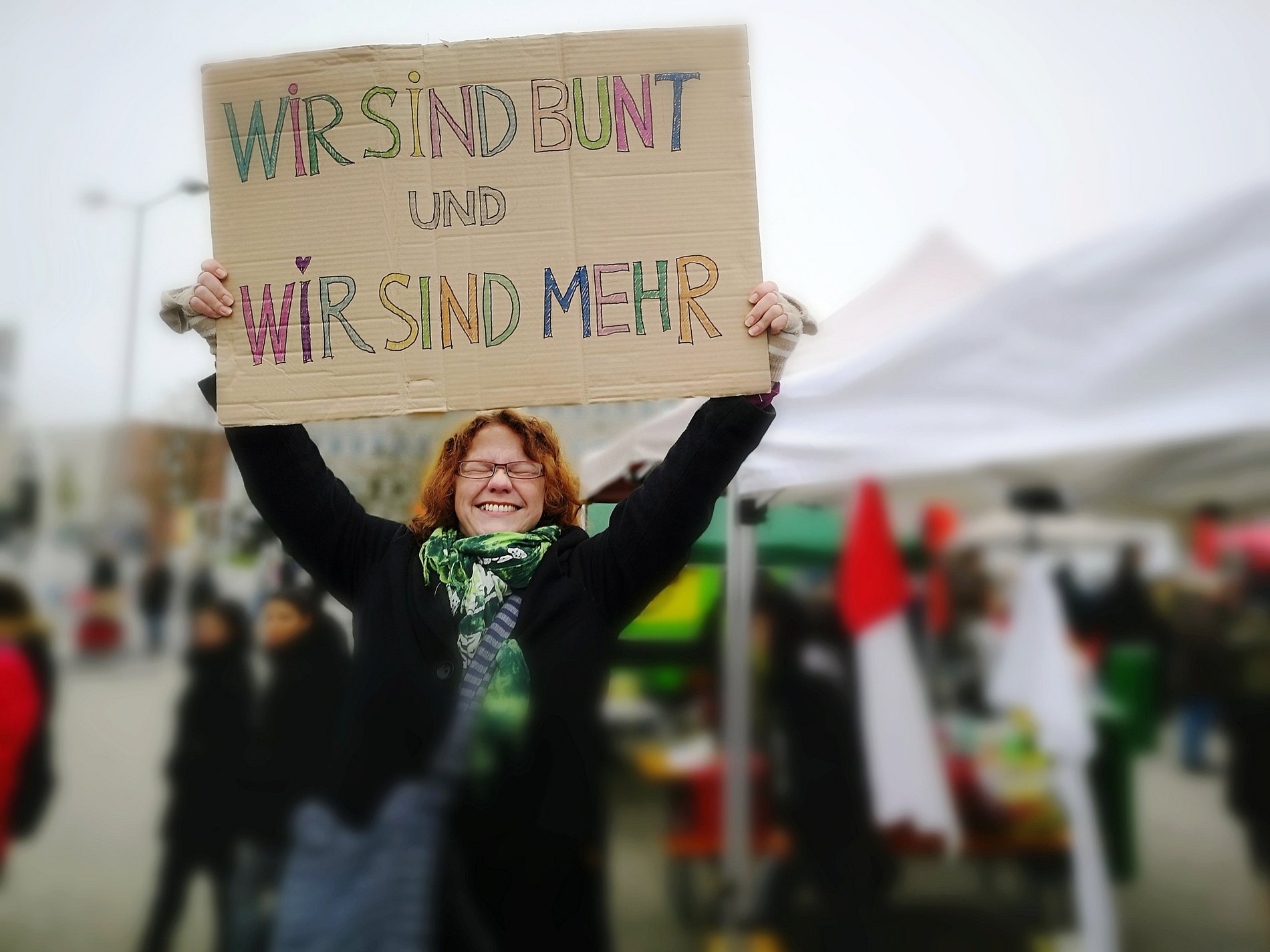 Eine Frau, Augen geschlossen und lachend, hält mit beiden Händen ein Kundgebungsplakat in die Höhe.