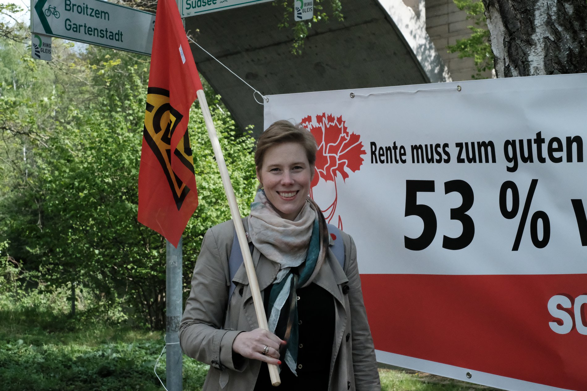 Eine Gewerkschaftlerin mit roter Fahne vor einem Plakat in Braunschweig.