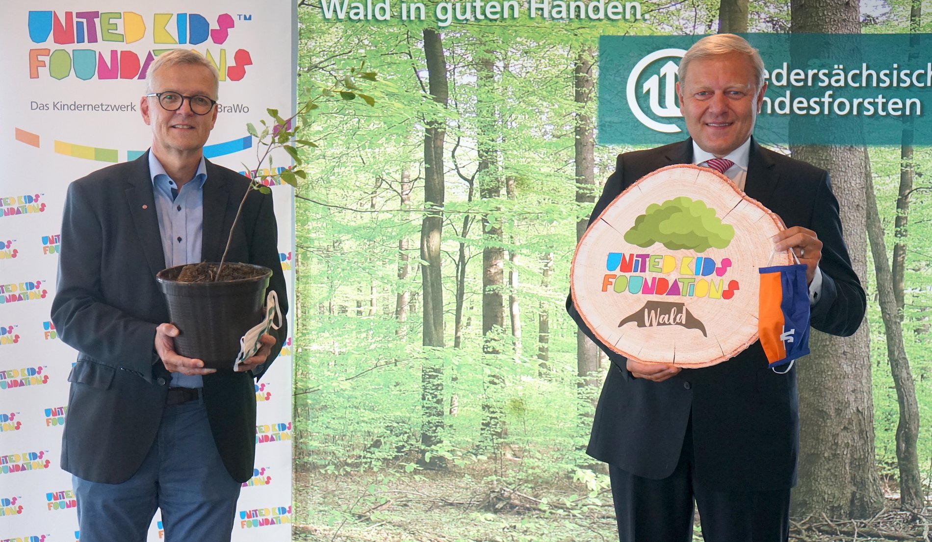 Dr. Klaus Merker und Jürgen Brinkmann vor einer Leinwand mit Wald und dem Logo der United Kids Foundation.