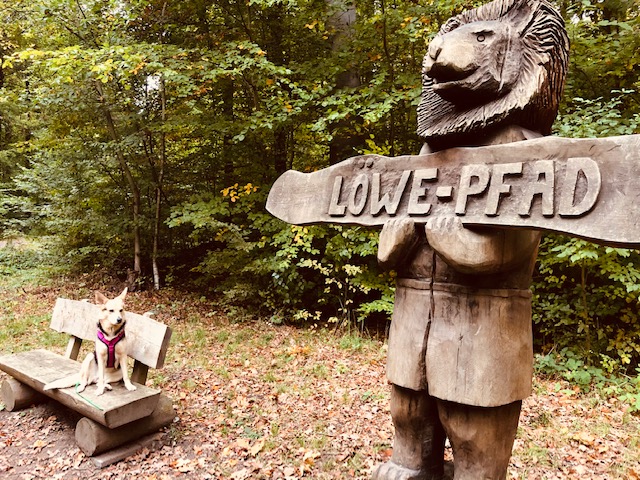 Ein hölzernes Weg-Hinweisschild mit einem Löwenkopf.