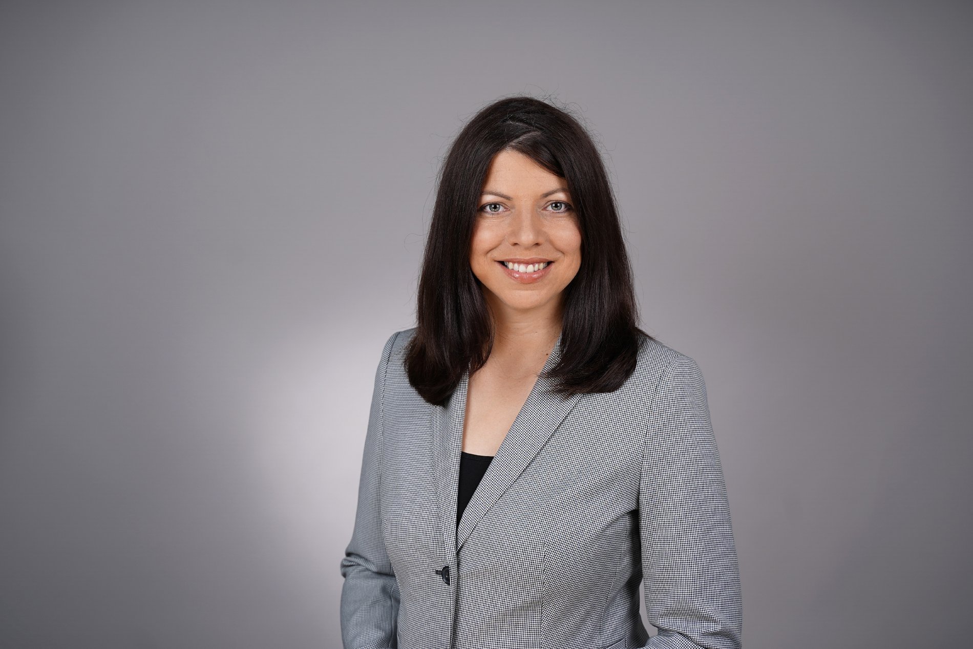 Eine brünette Frau im Blazer vor grauem Hintergrund.