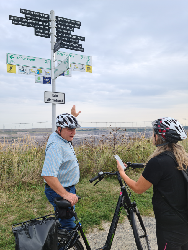 Eine Mann mit Fahrrad zeigt auf einen Wegweiser.