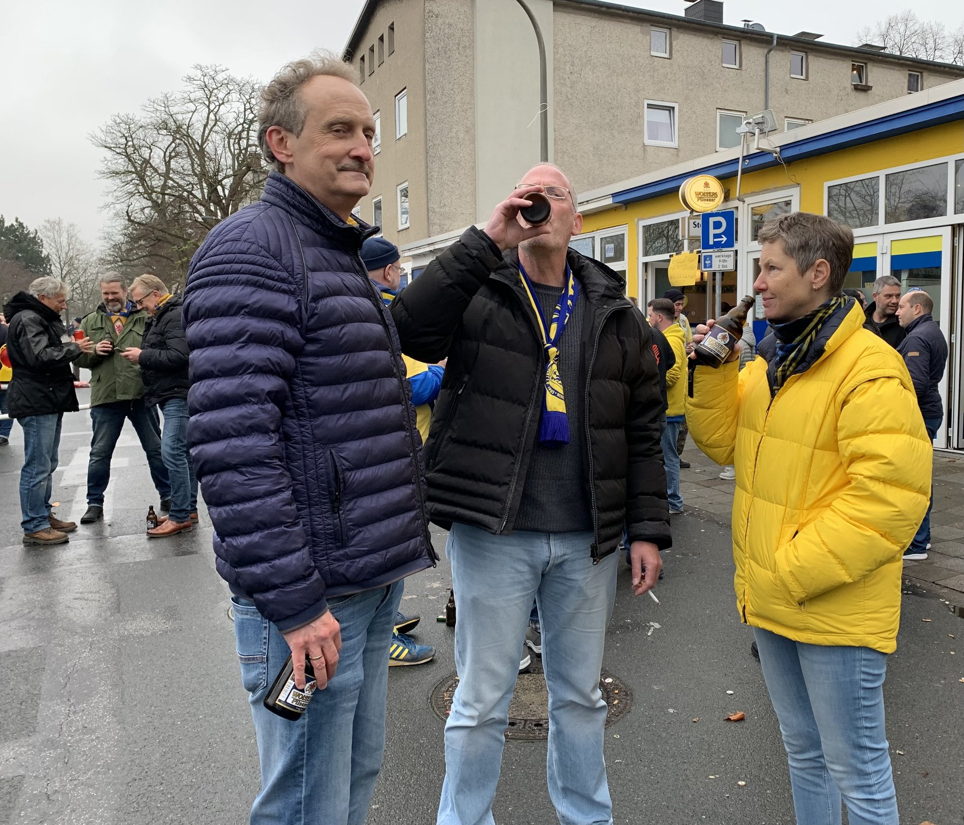 Drei Personen stehen vor einem Stadion.