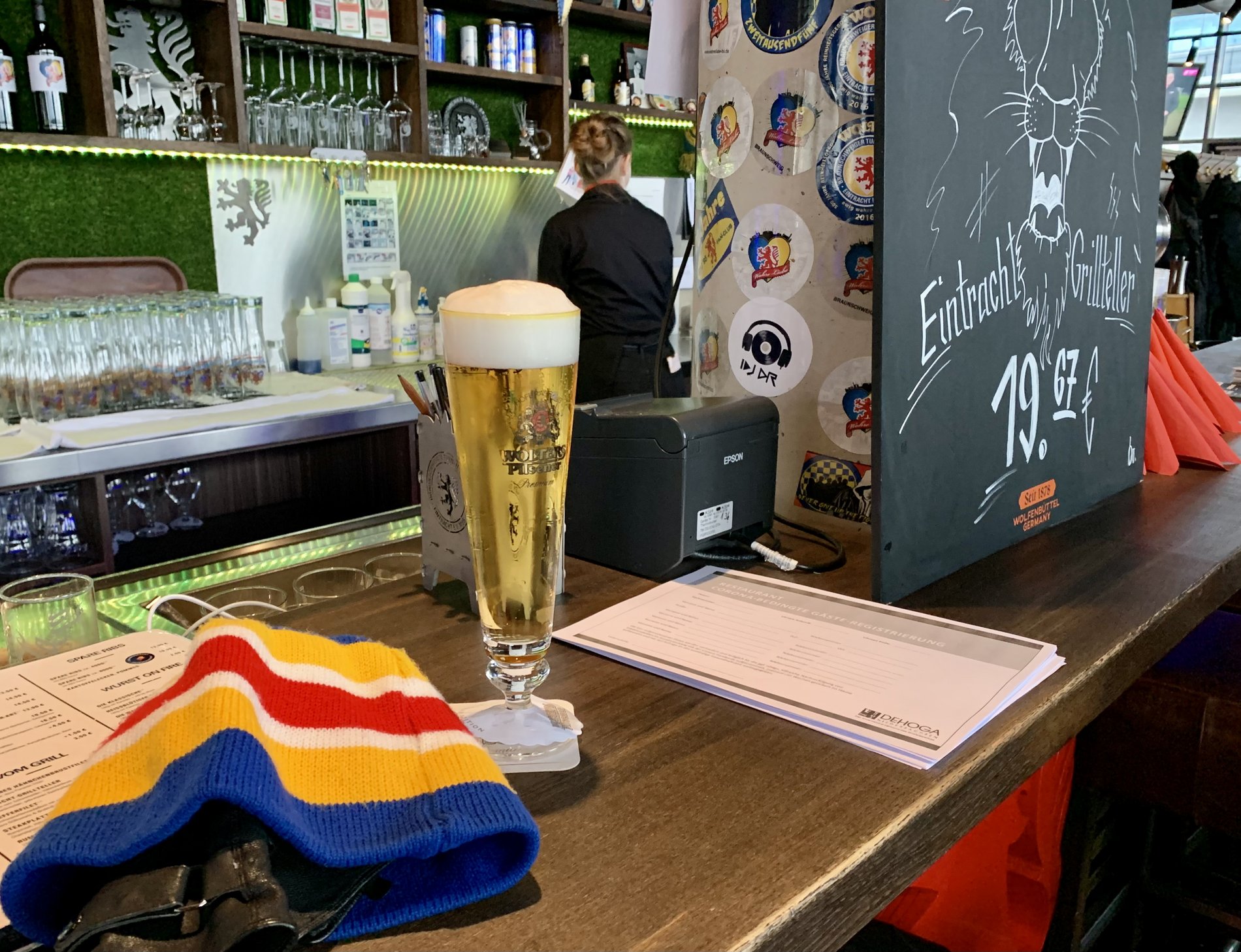 Ein Schal, ein Schreibblock und ein Glas Bier liegen auf einer Theke.