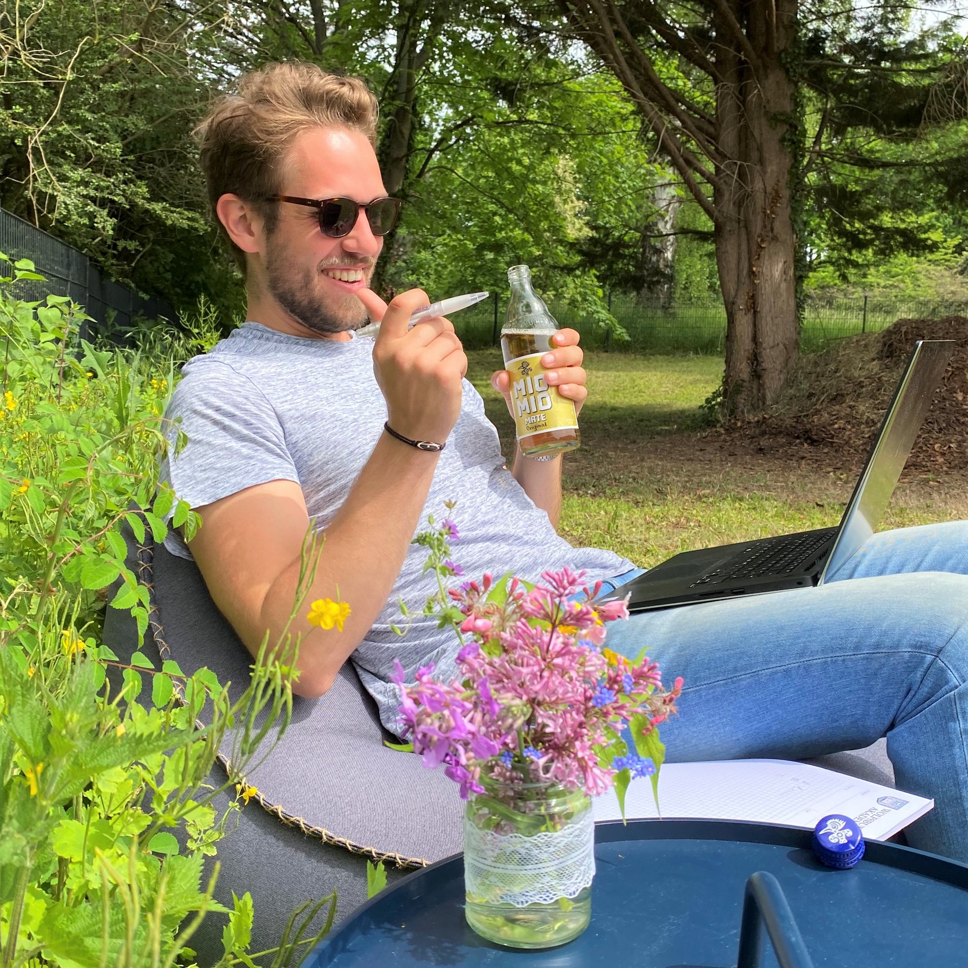 Ein Man sitzt mit einem Laptop auf dem Schoß in einem Garten.