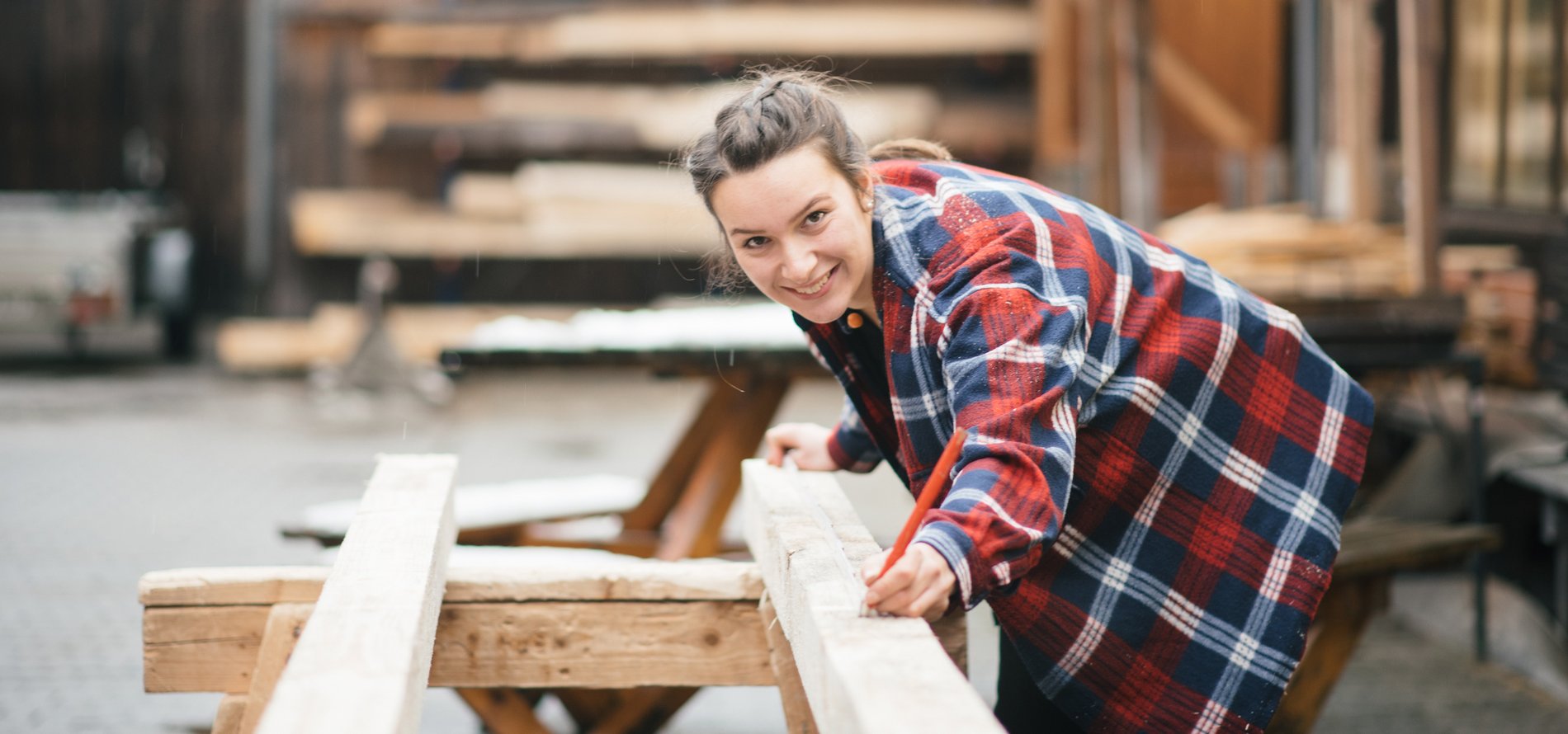 Eine Frau bearbeitet einen Holzbalken in einer Werkstatt.