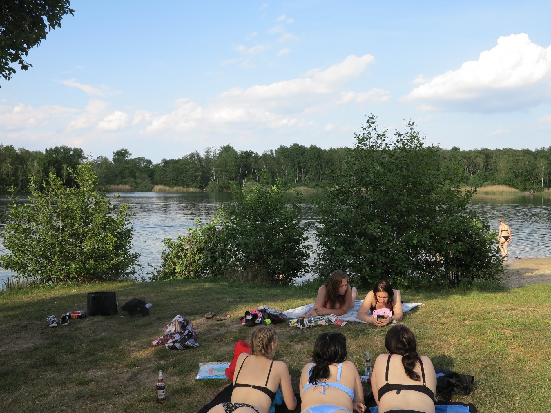 Einige Frauen liegen auf einer Wiese vor einem Badesee.